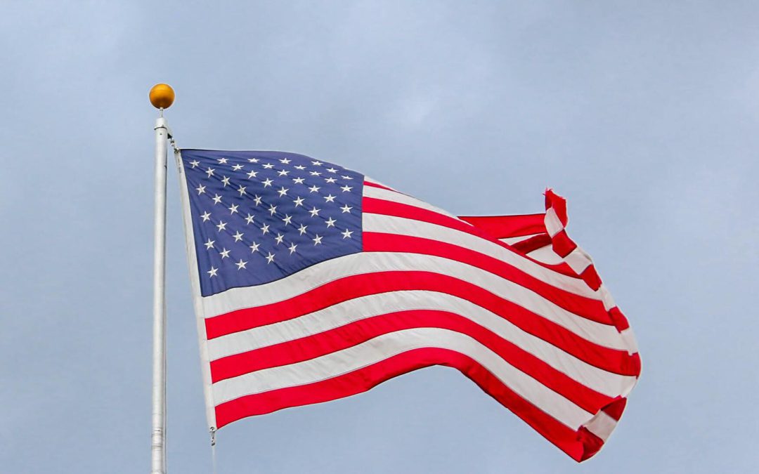 A United States flag blowing in the wind under a clear blue sky.